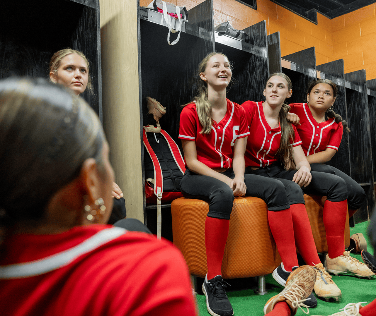Softball players sitting in a locker room.